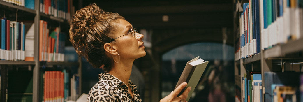 A researcher looks for a book among a library shelf.