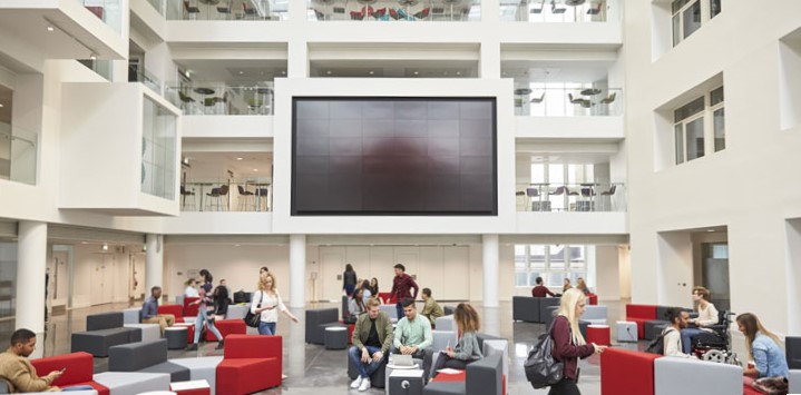 Students meeting in a large common area in a modern university building foyer.