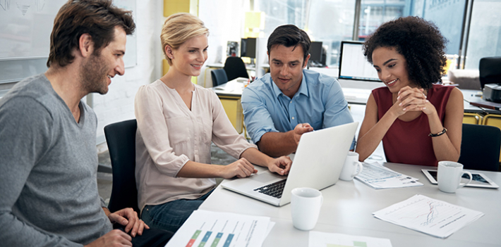 A group of four people sitting around a laptop.