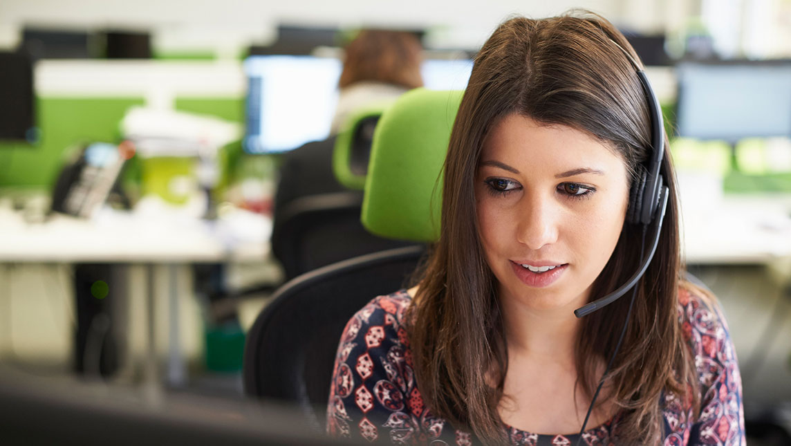 A member of staff in an office uses a headset to talk with a student during GCSE results day.