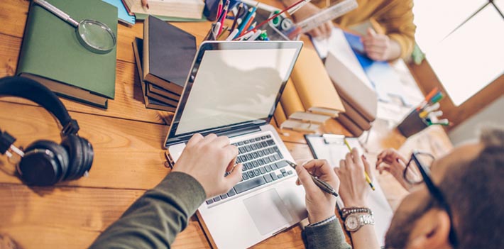 Students sitting around a desk using books and laptop.