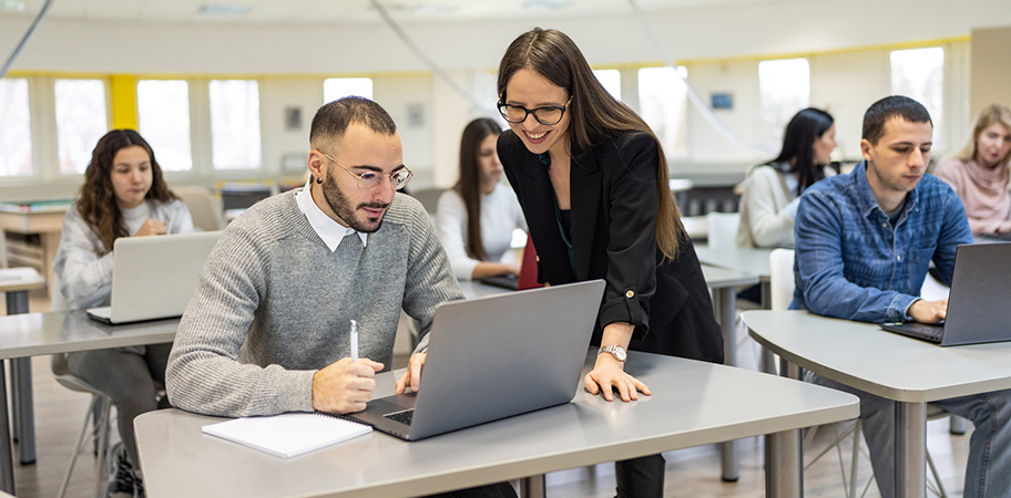 A female tutor helping a male student with a laptop.