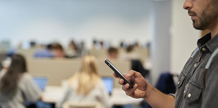 A man looking at his phone in a classroom.