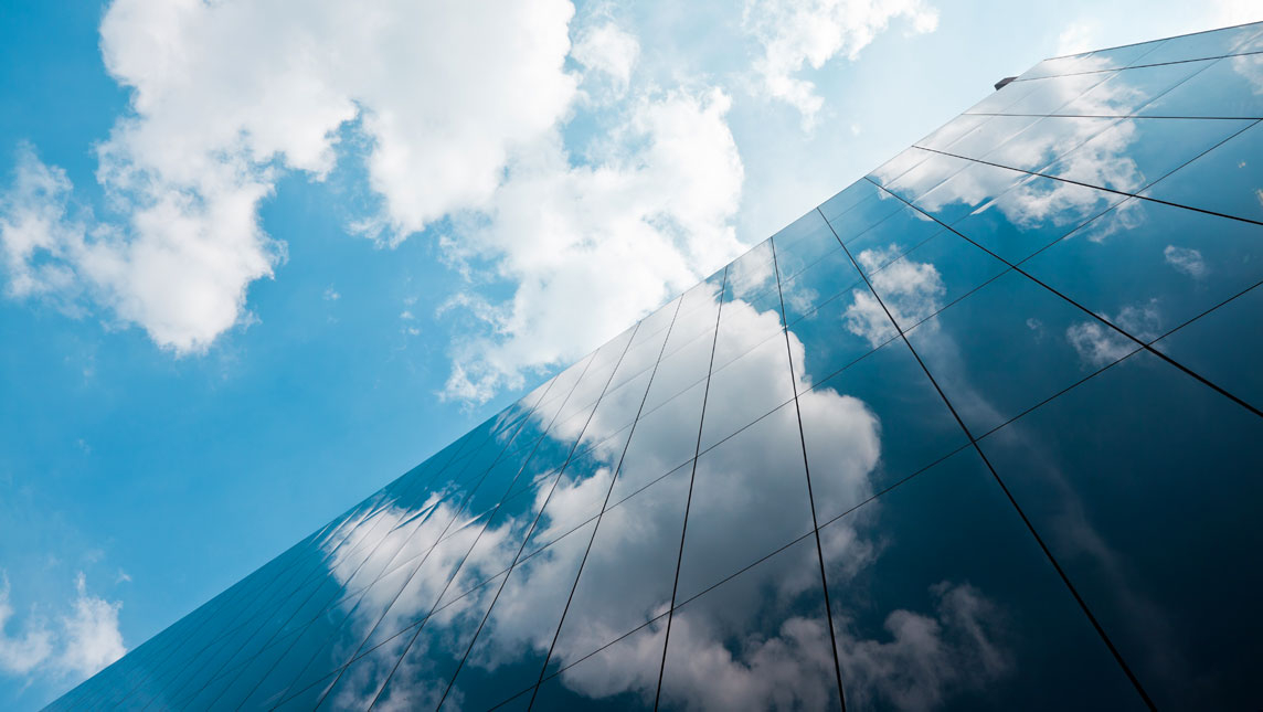 A bright sky full of clouds is reflected on a modern glass skyscrapper.