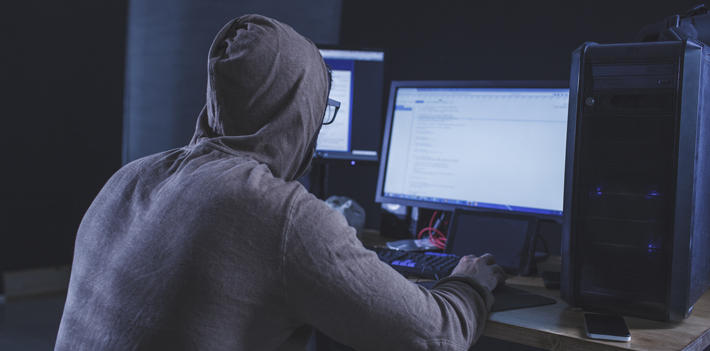 Computer hacker wearing hooded shirt using computer at table