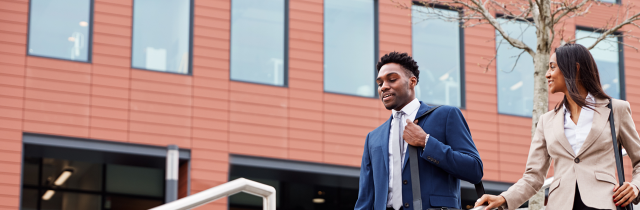 Two graduates walk down stairs outside their office building.