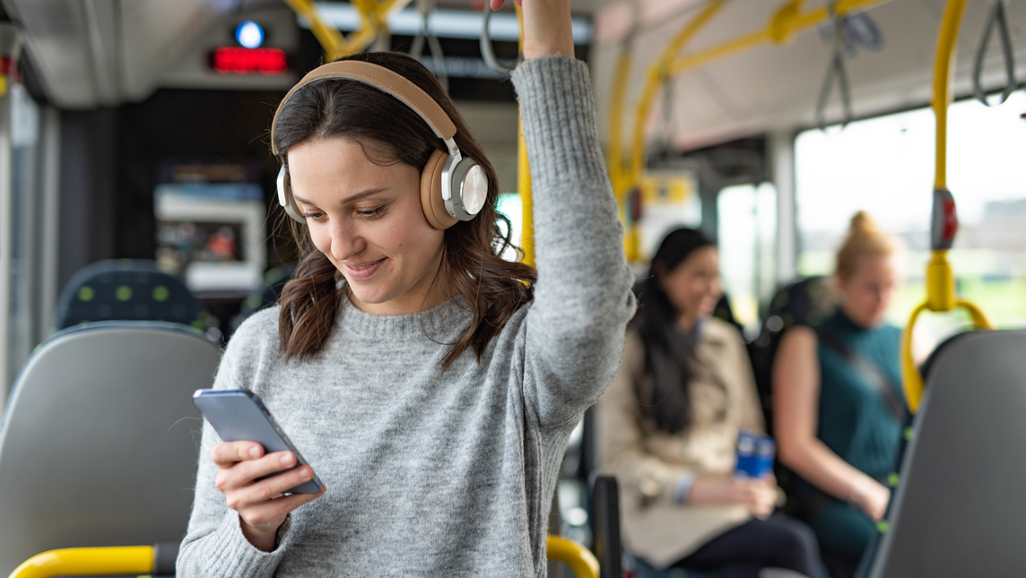 Happy woman using mobile phone and headphones while listening a music in a bus