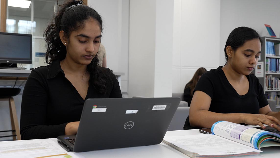 Two students using laptops in a classroom.