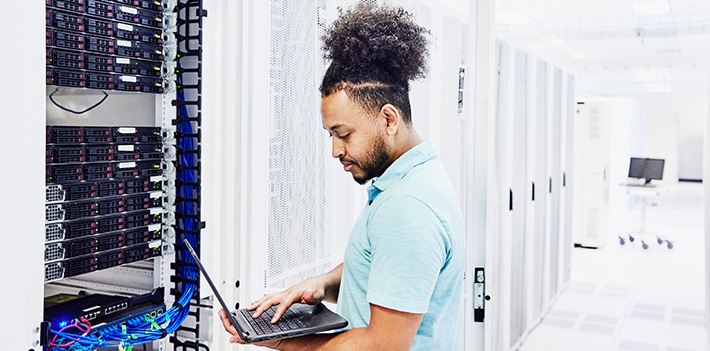 IT professional looks at a laptop while working on a server in a data centre.
