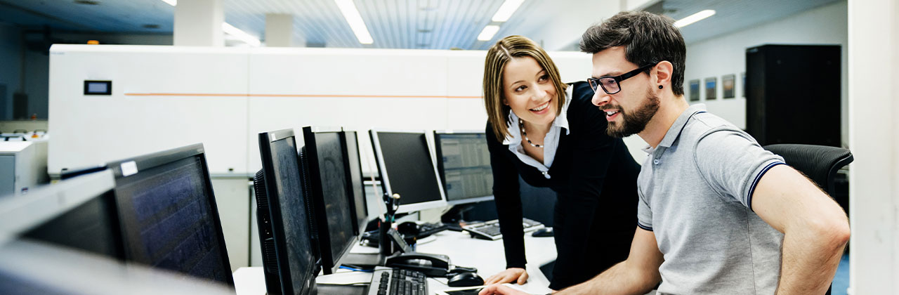 A consultant talks with a customer in front of computer screens.