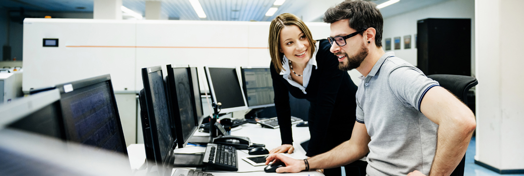 A consultant talks with a customer in front of computer screens.