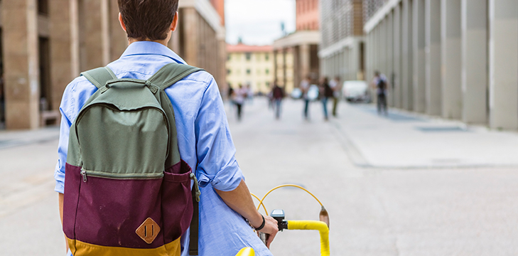 Student with a backpack and bicycle wanders through town.