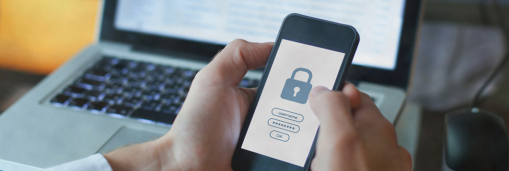 Two step authentication: a person holds a mobile phone in front of a lap while putting in their login details.