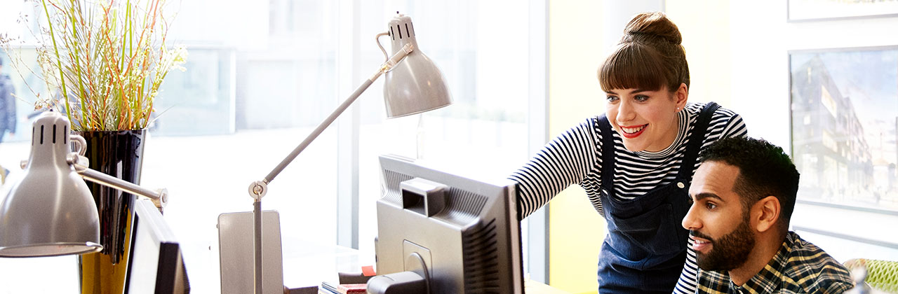 Two co-workers point at a computer screen.